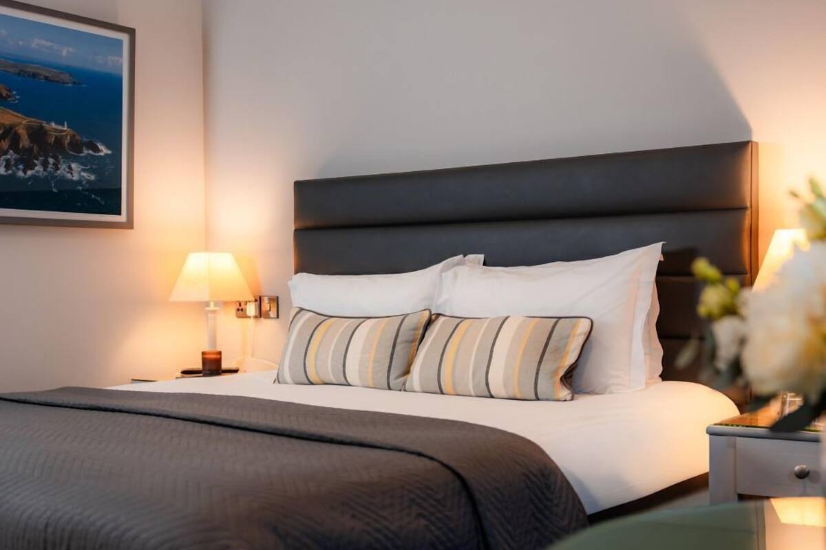 A neatly made bed with a dark headboard, a lamp, and a framed picture on the wall.