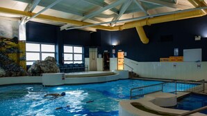 An indoor swimming pool with clear water, a diving board, and a lifeguard chair.
