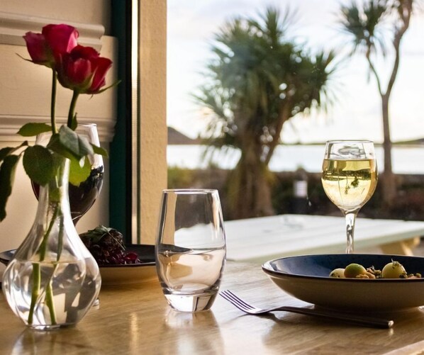 A dining table with a vase of roses, a bowl of fruit, and a glass of white wine. - Celtic Ross Hotel (Rosscarbery)