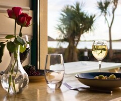Una mesa de comedor con un jarrón de rosas, un cuenco de fruta y una copa de vino blanco.