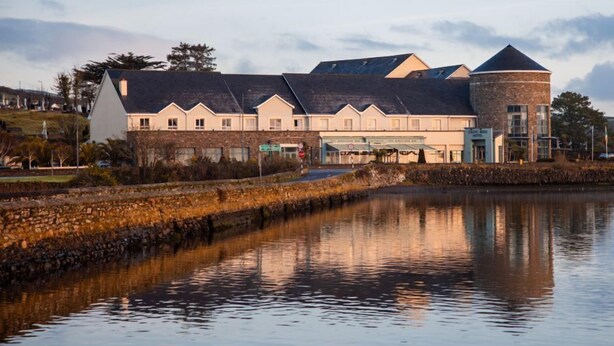 A hotel with a long, low-roofed building and a round tower, situated beside a calm body of water.