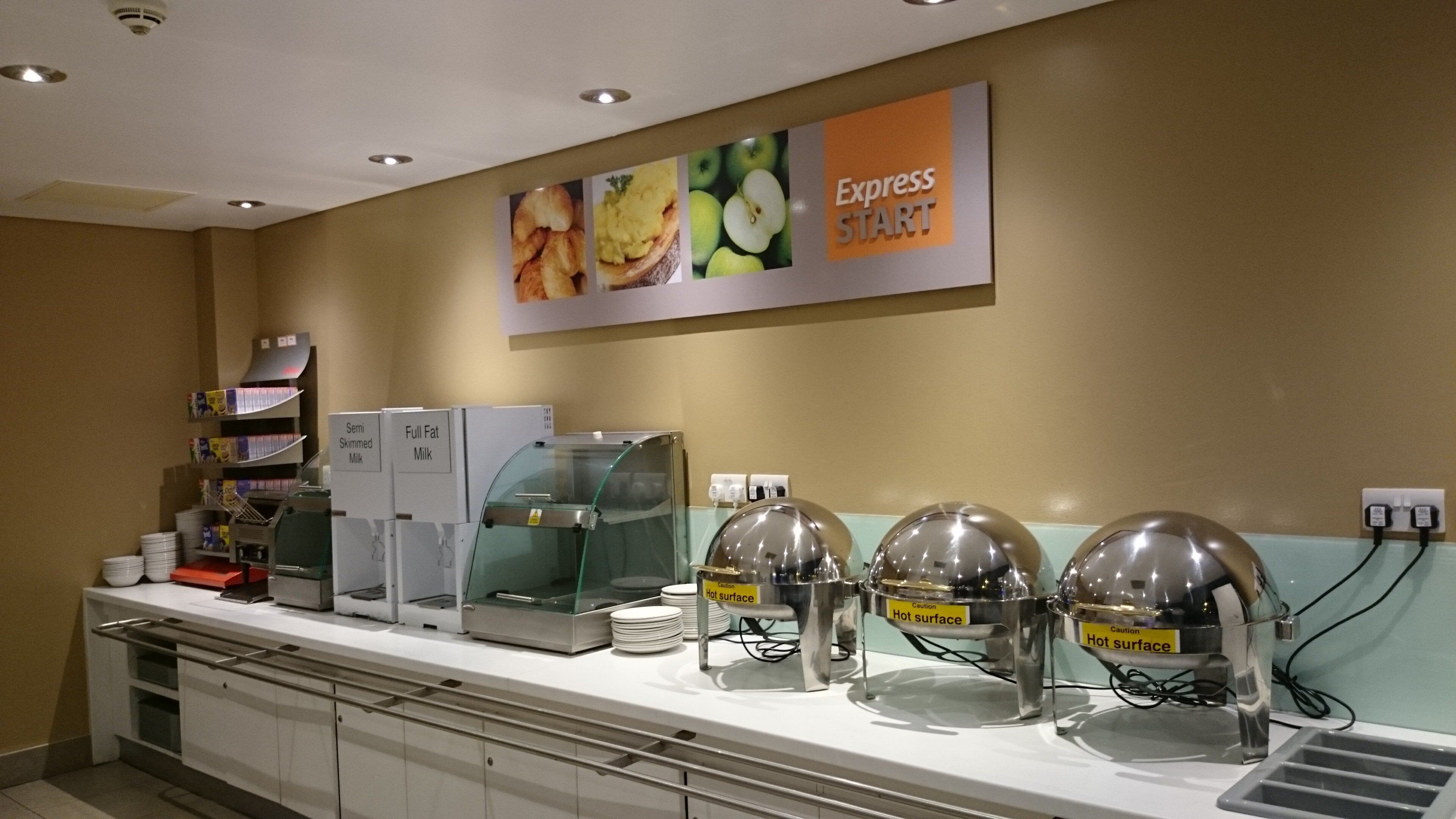 Zona de bufé con varios dispensadores de alimentos, incluyendo opciones de leche, y un cartel para Express START.
