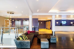 A modern lobby with a reception desk, a staircase, and a seating area with a sofa and ottomans.