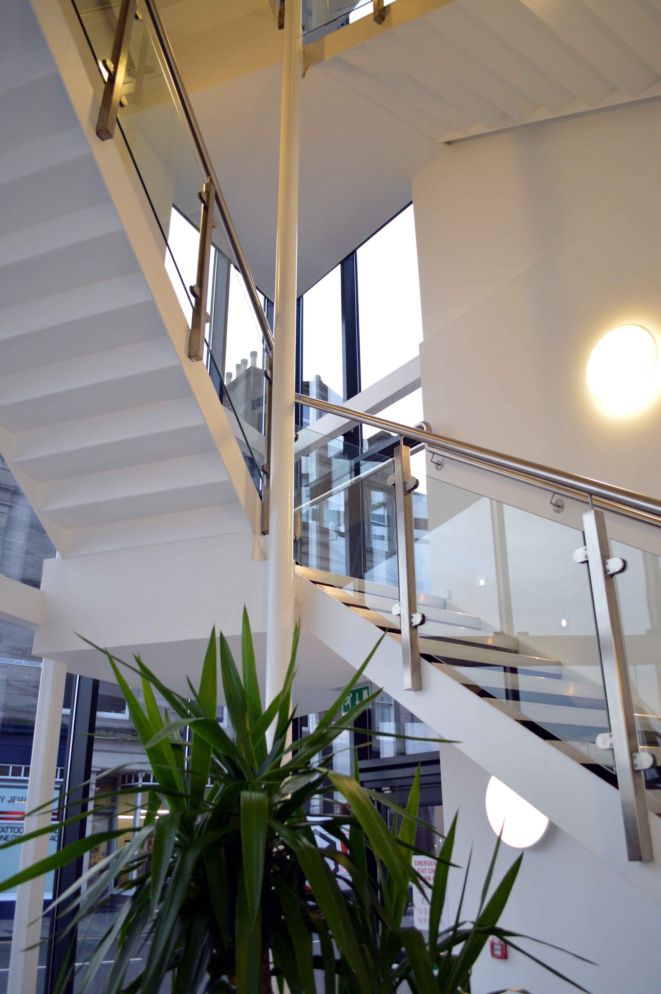 Un interior moderno con una escalera de cristal, barandillas de metal y una planta en maceta.