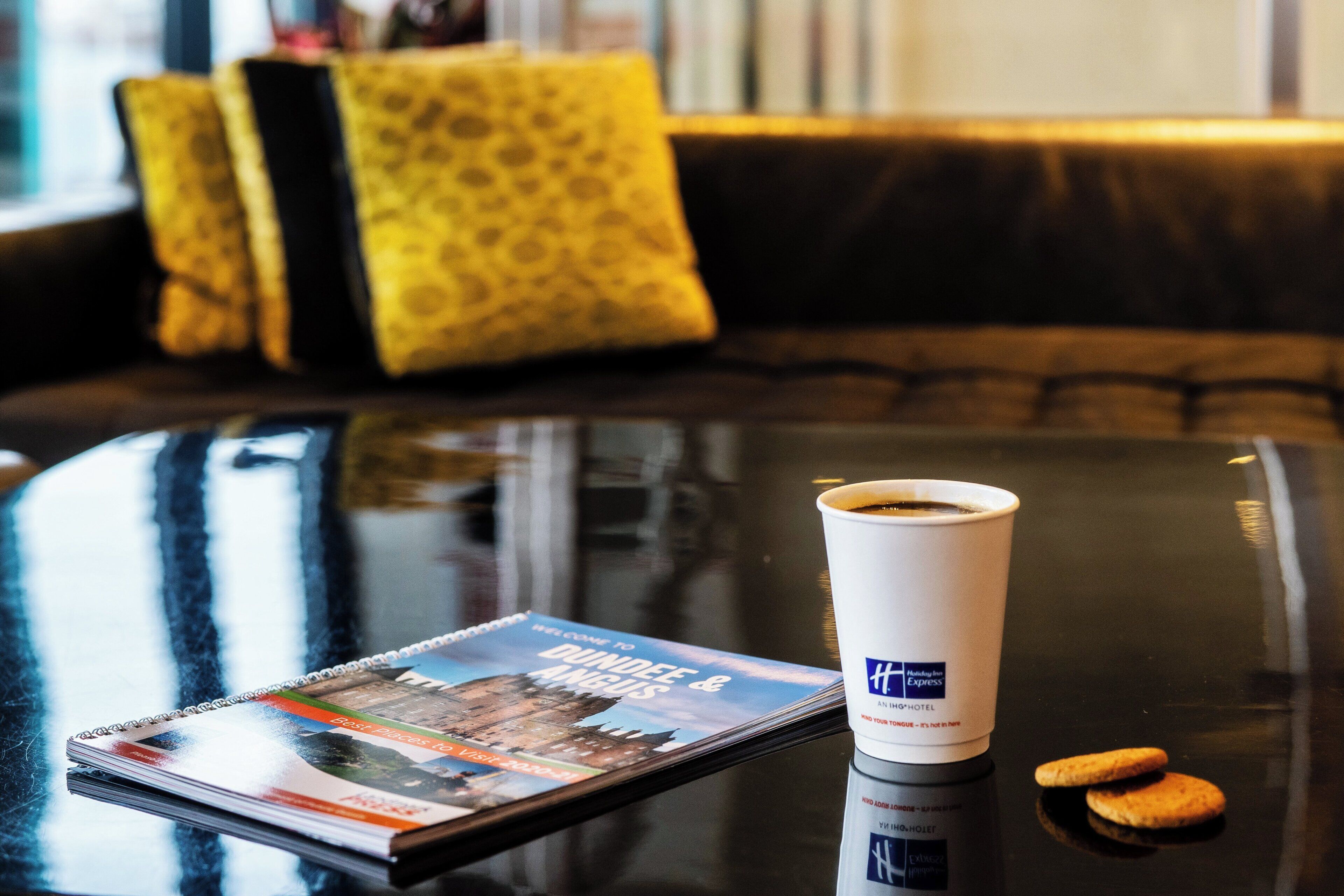 Une tasse de café, un dépliant touristique et un biscuit sur une table en verre.