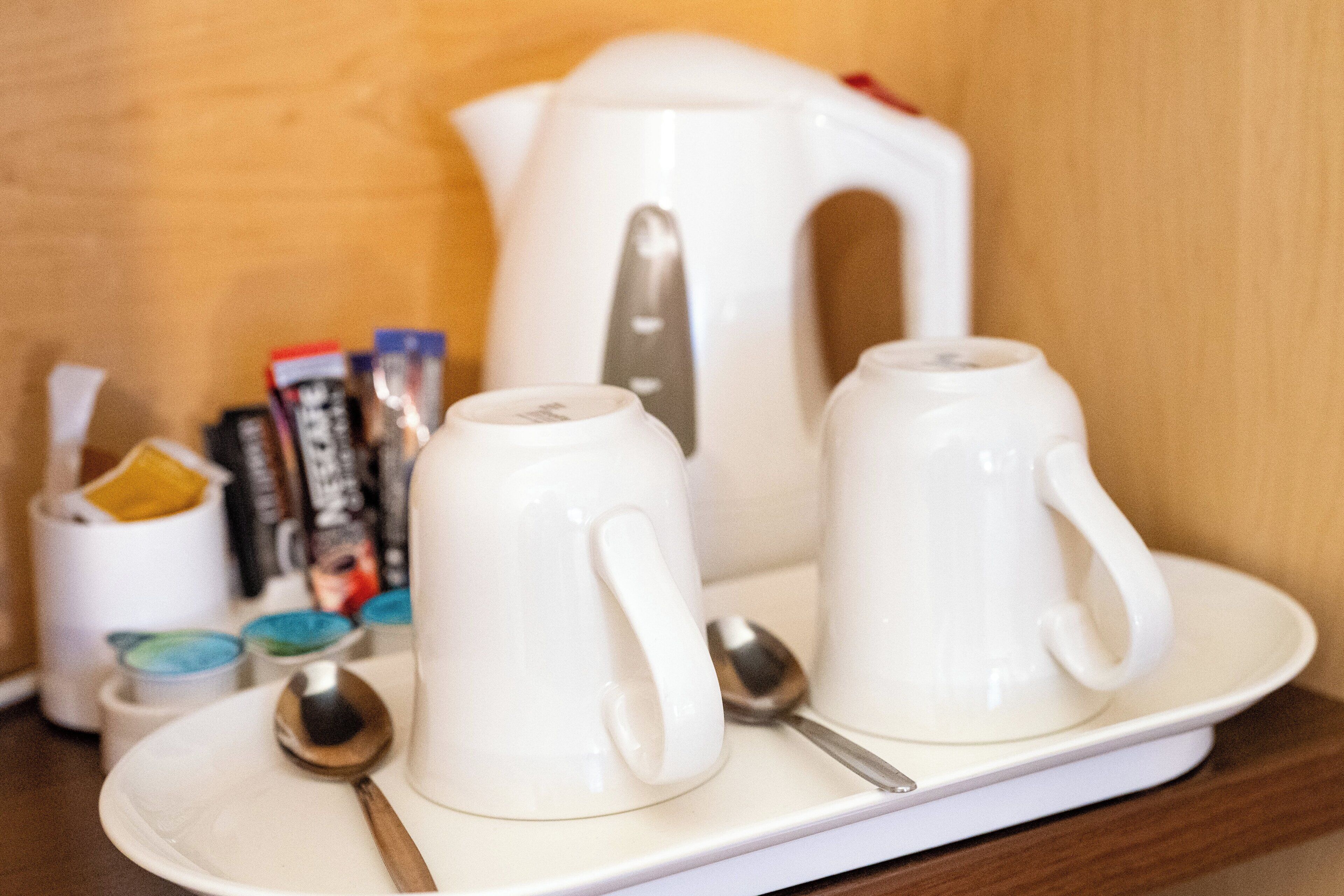 A tray with two white mugs, a white teapot, and a white cup with a spoon on a wooden surface.