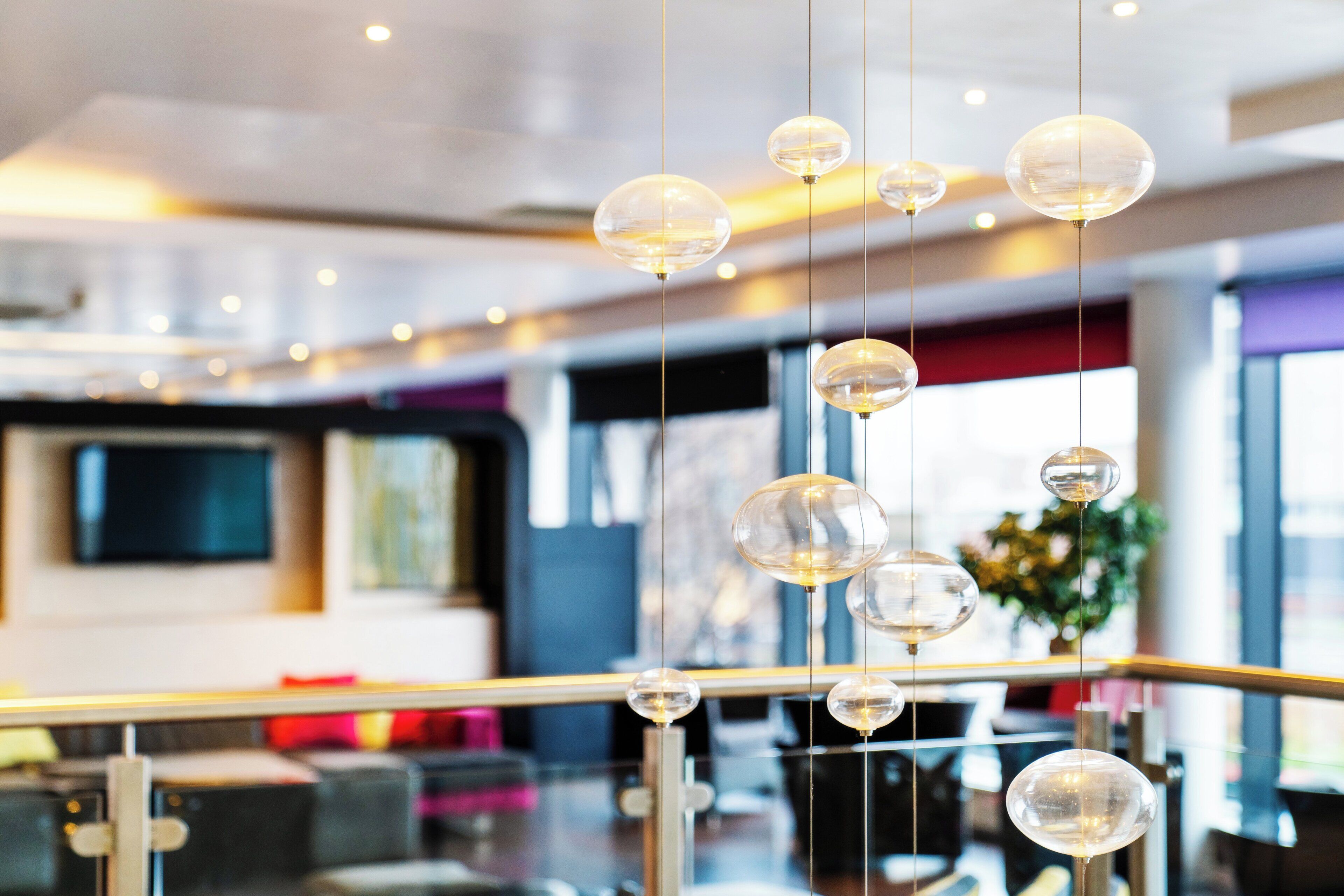A modern interior with hanging spherical light fixtures, a glass railing, and a blurred background suggesting a spacious area.