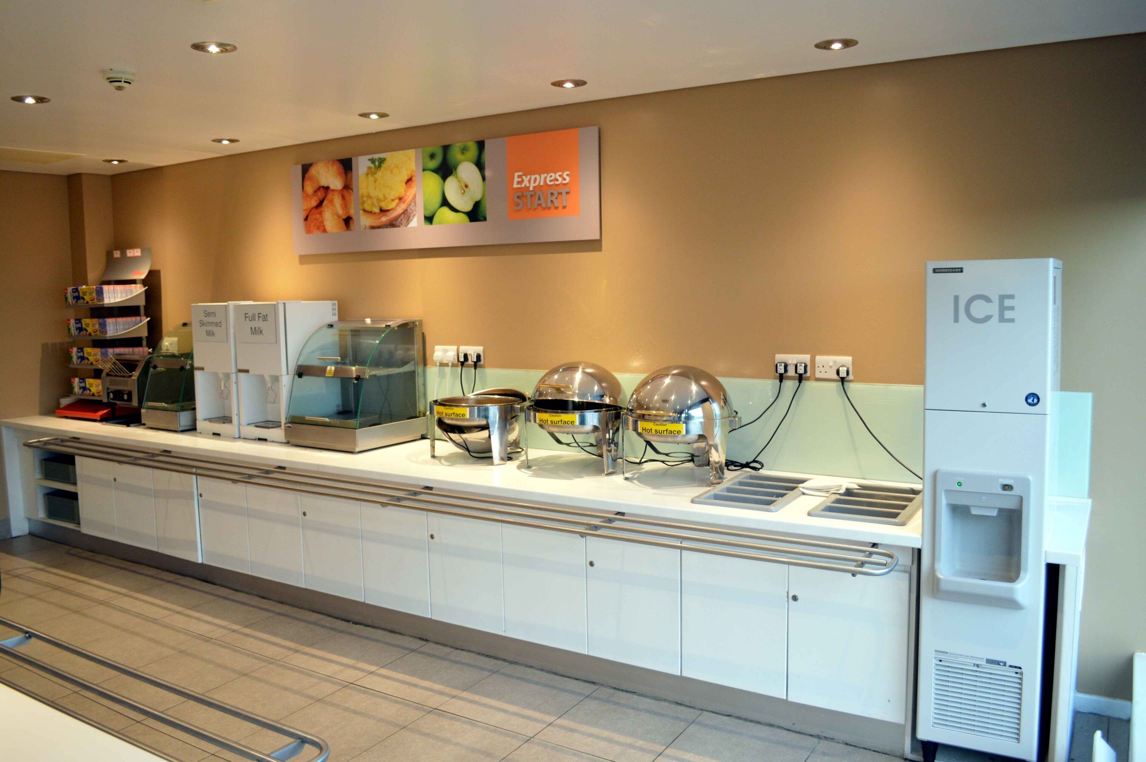 A buffet area with various food dispensers, a refrigerator, and a water dispenser.
