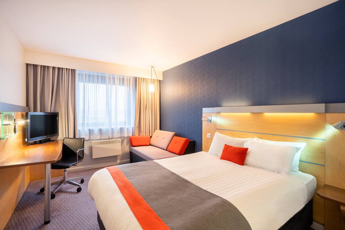 A hotel room with a large bed, a desk with a computer, a sofa, and a TV.