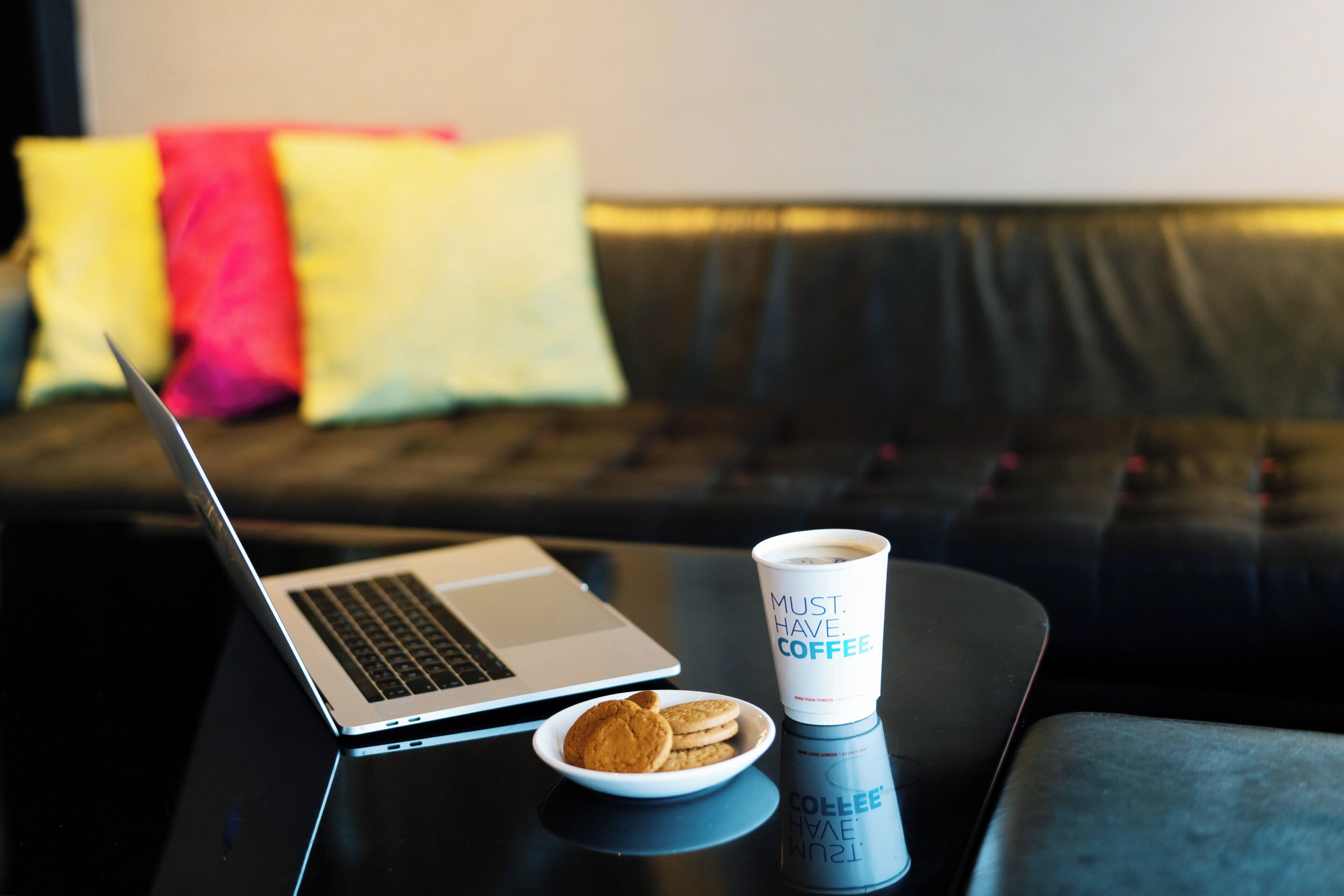 A laptop on a table with a cup of coffee and a plate of cookies.