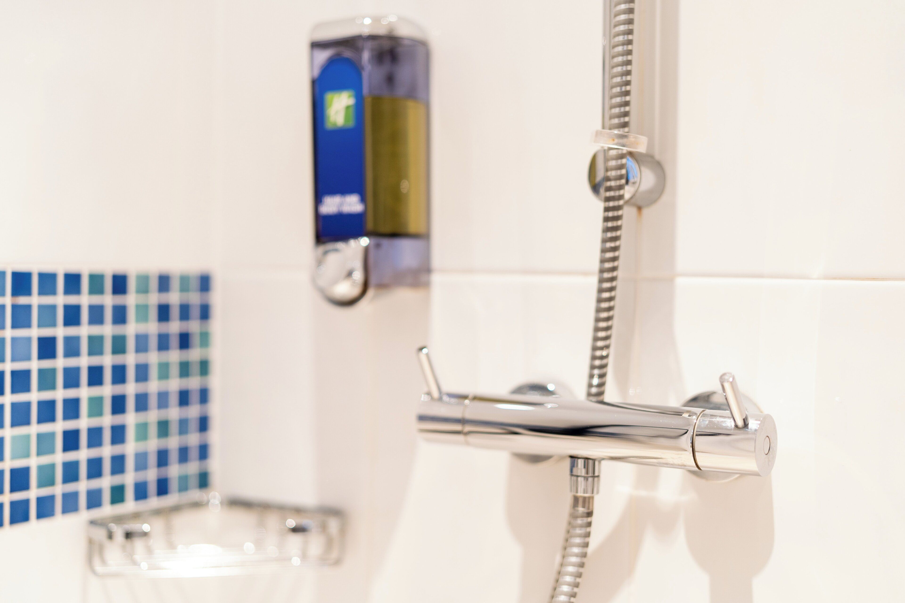 Un bagno con doccia, erogatore di sapone e parete rivestita in piastrelle.