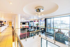 A modern hotel lobby with a reception desk, seating area, and a glass railing overlooking a cityscape.