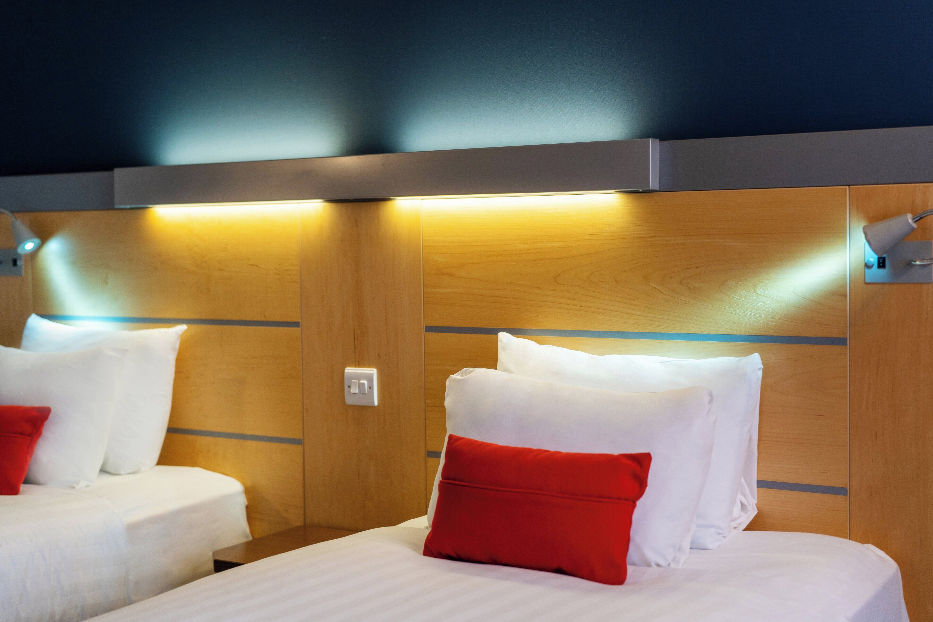 Habitación de hotel con dos camas, cada una con ropa blanca y almohadas rojas, y cabeceros de madera.
