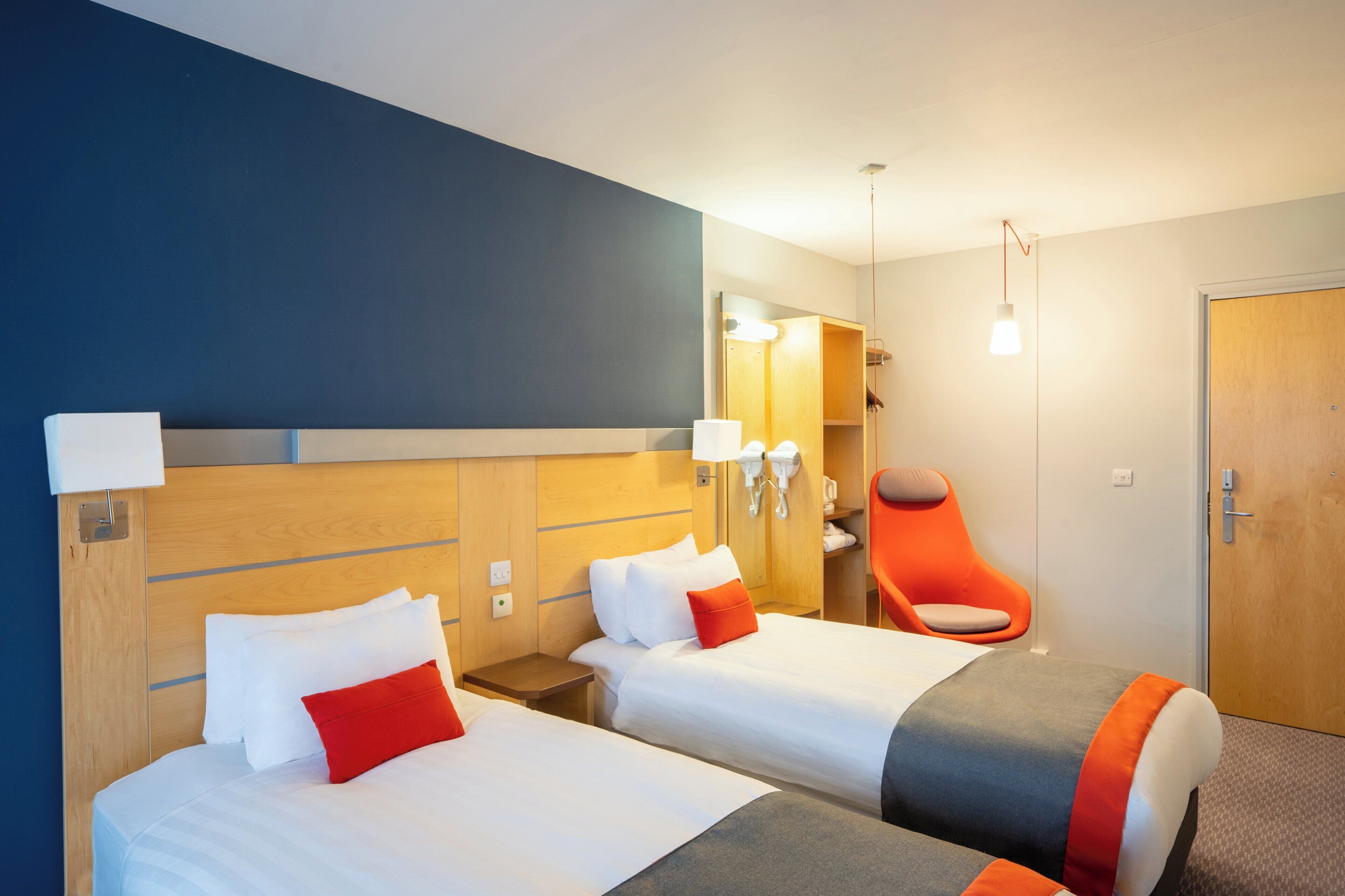 Une chambre d’hôtel avec deux lits, une chaise, un miroir et une porte.
