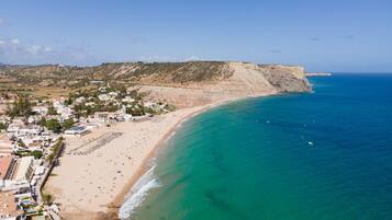 A coastal town with a long sandy beach, a rocky cliff, and a clear blue sea.