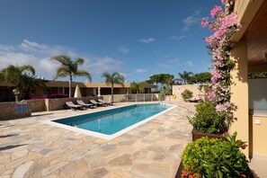 Piscina con sillones de descanso, rodeada de baldosas de piedra y plantas en macetas.