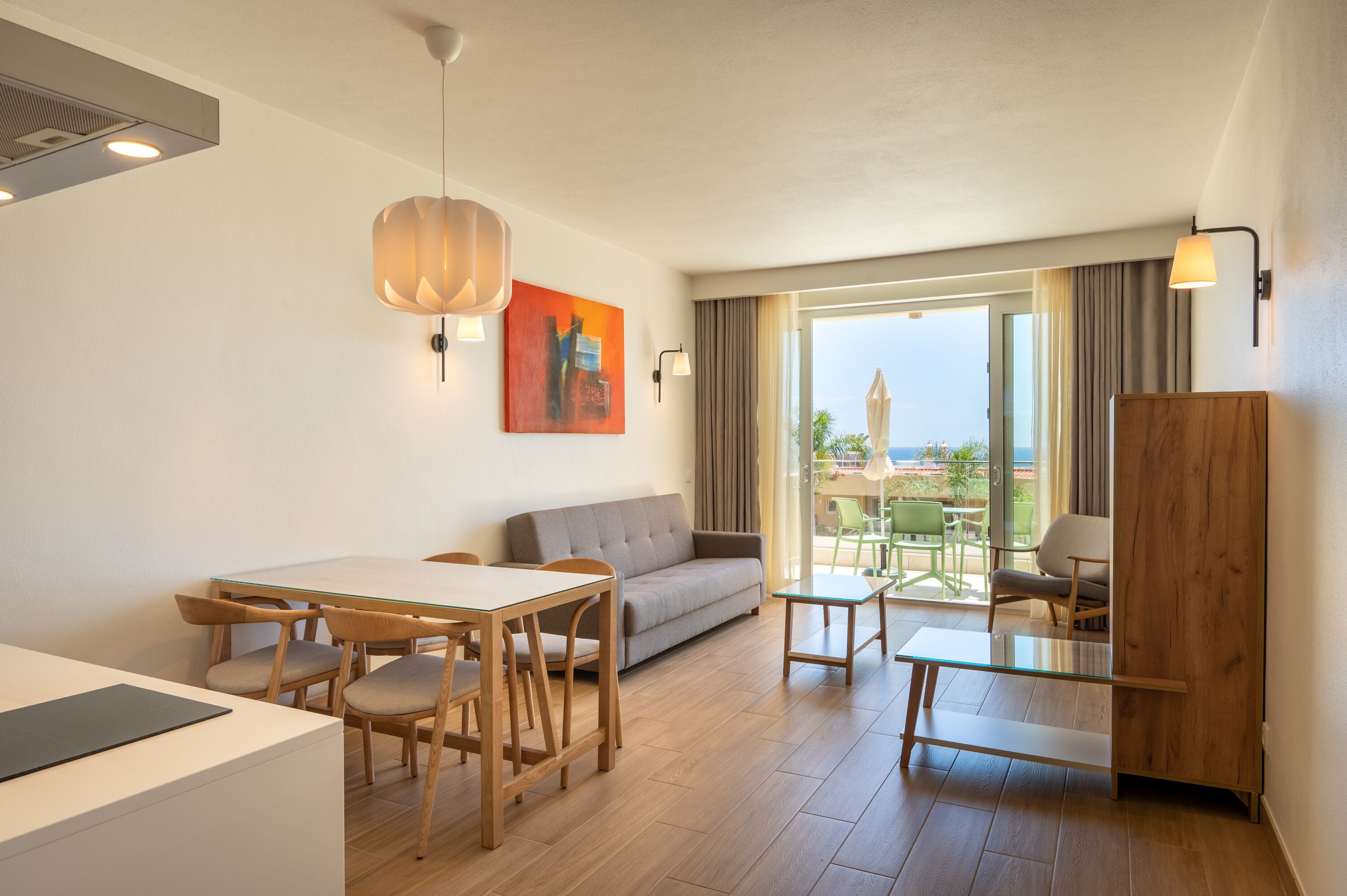A modern hotel room with a dining area, a sofa, and a balcony with a view.