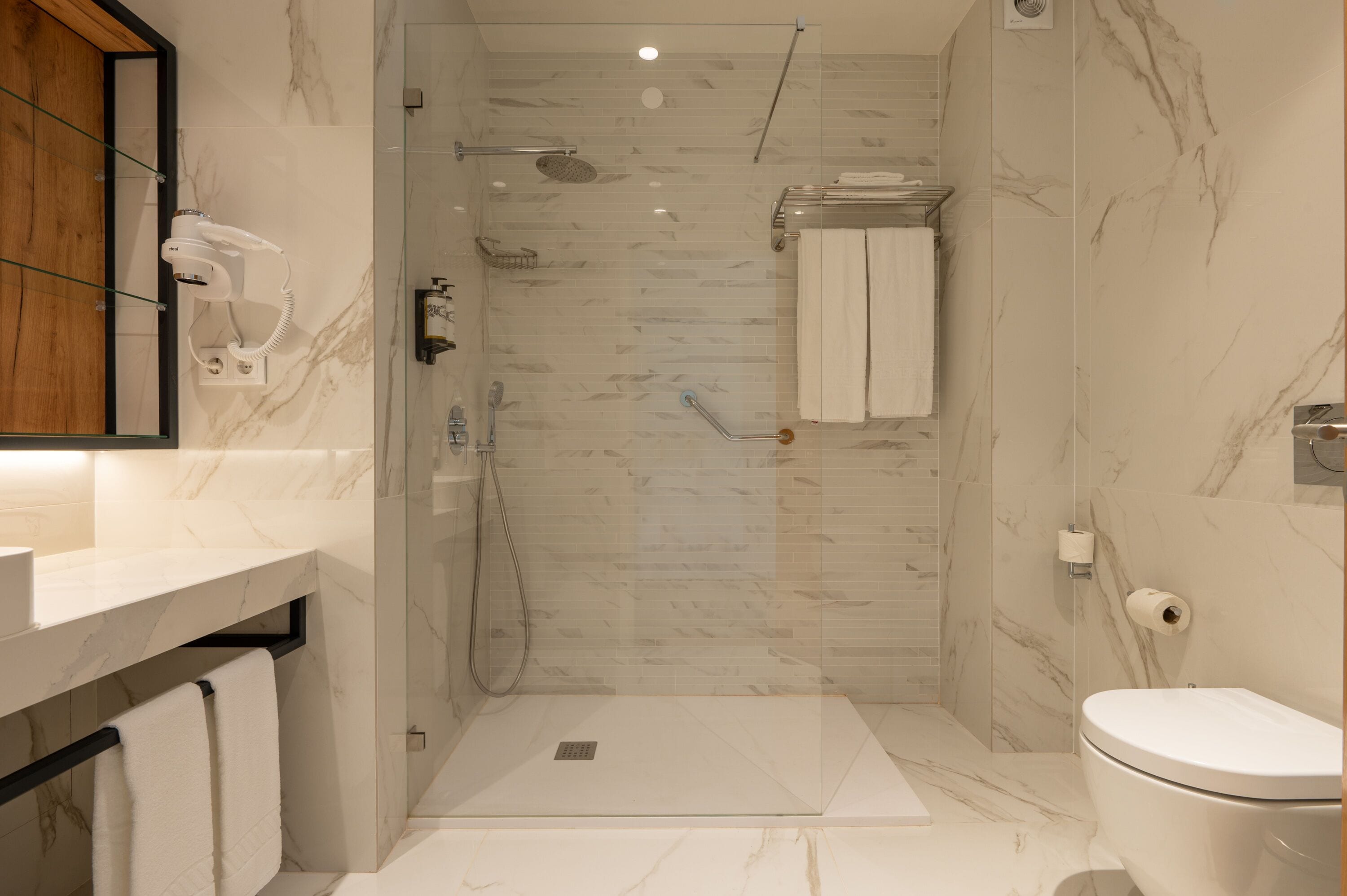 A modern bathroom with a glass-enclosed shower, a toilet, and a sink with a towel rack.