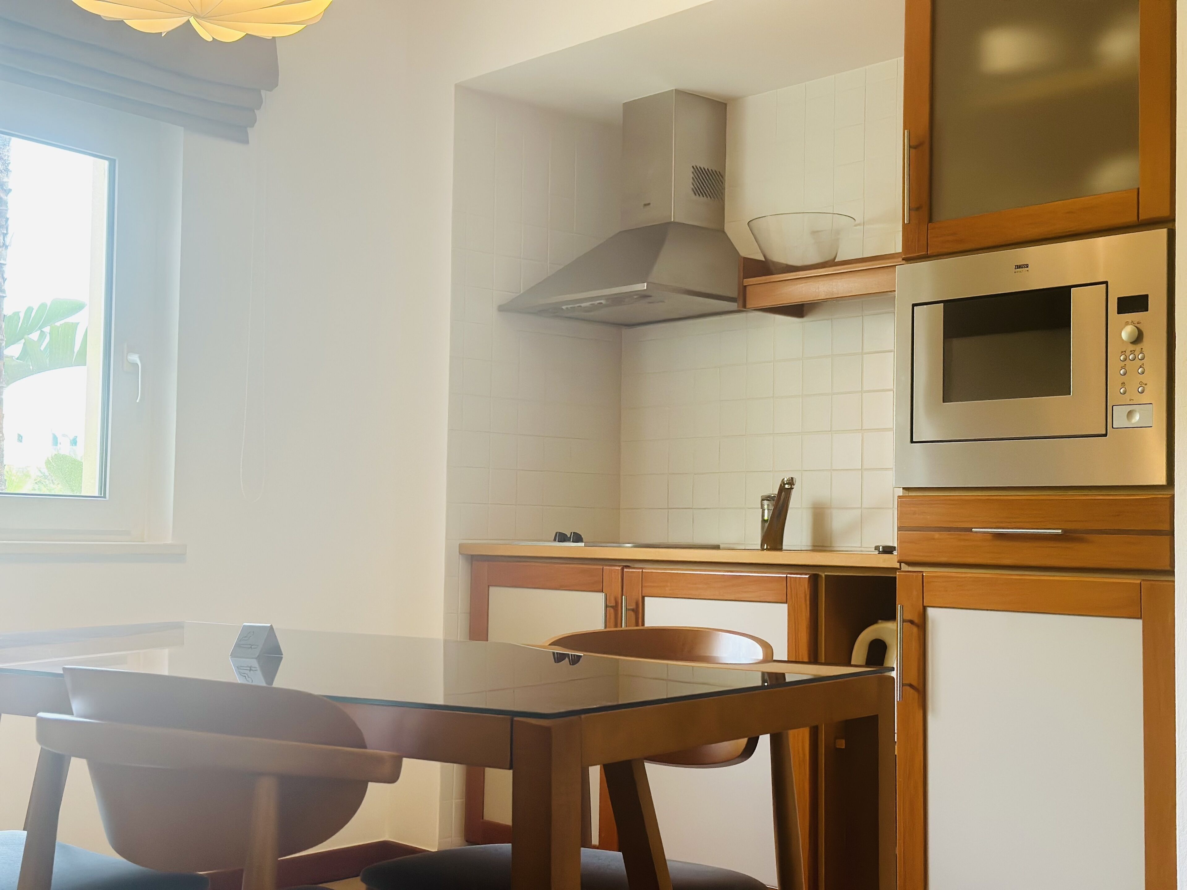 A kitchen with a glass table, wooden chairs, a microwave, and a stove.