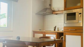 A kitchen with a glass table, wooden chairs, a microwave, and a stove.