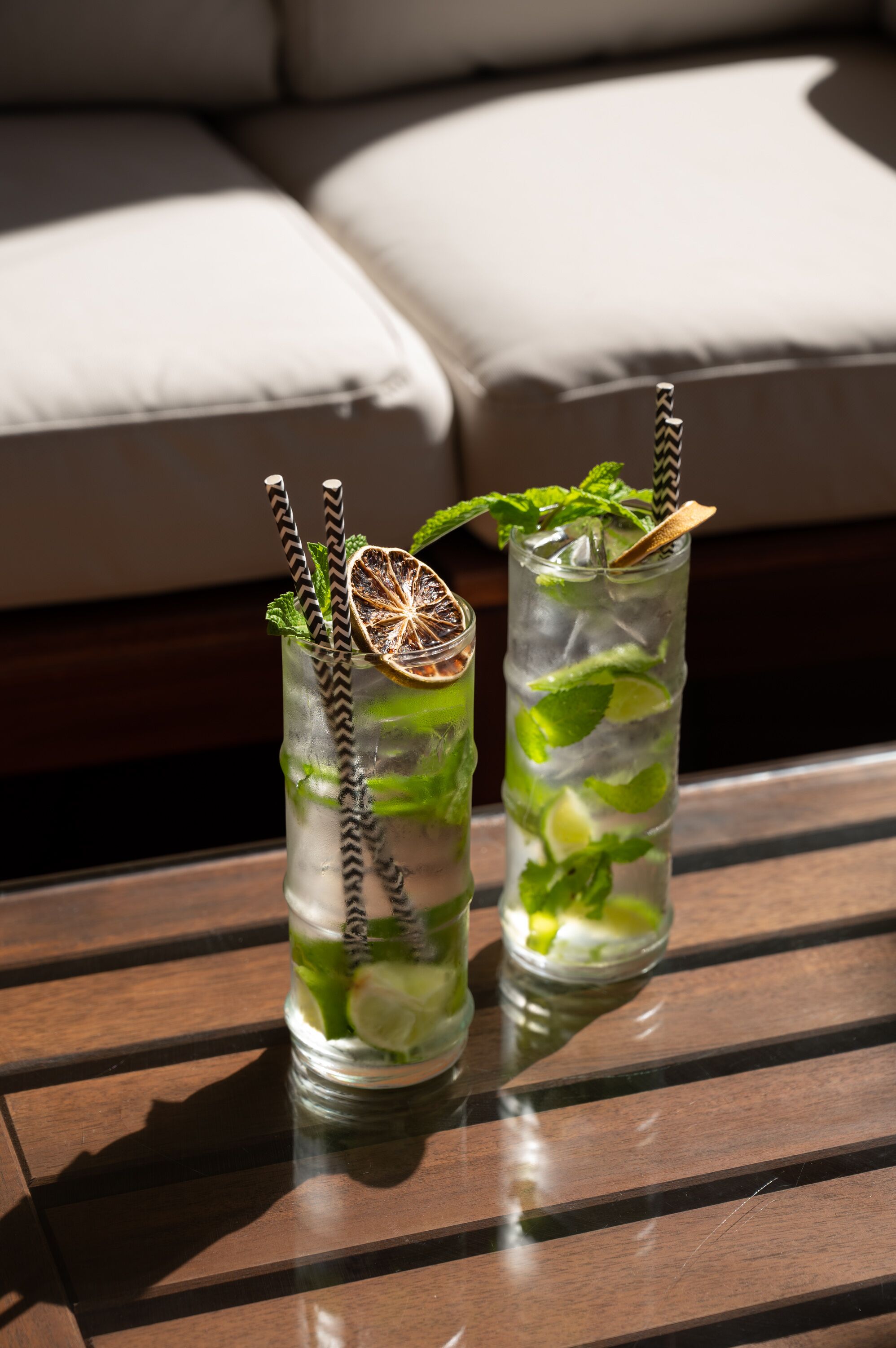 Deux grands verres remplis d’une boisson rafraîchissante à la menthe et au citron vert, posés sur une table en bois.