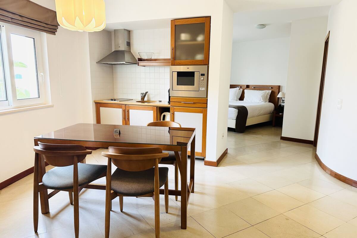 A compact kitchen with a microwave, stove, and wooden cabinets. There is a dining area with a table and chairs.