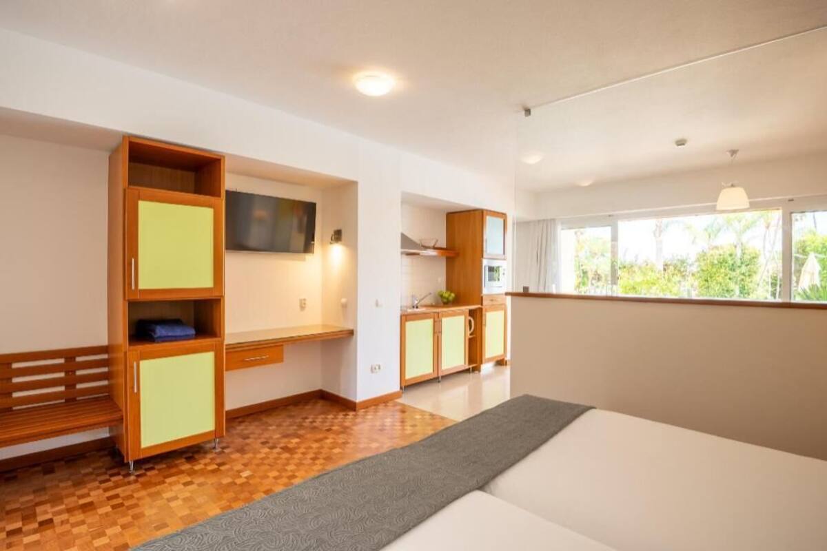 A modern room with a wooden bench, a TV, a kitchenette, and a large window.
