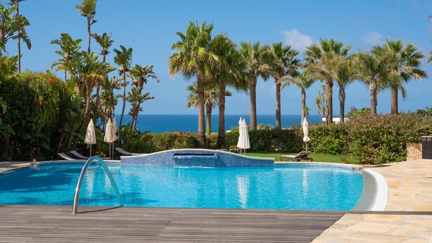 A swimming pool with a view of the ocean, surrounded by palm trees and lounge chairs. - Vila Luz (Lagos)