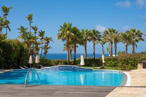 Una piscina con vistas al océano, rodeada de palmeras y sillas de descanso.