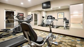 A gym with exercise equipment, a TV, and a mirror. - Pike Inn Le Roy - Bloomington Southeast Area (Le Roy)