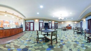 A spacious dining area with a patterned carpet, multiple tables and chairs, a counter with a display, and a television. - Pike Inn Le Roy - Bloomington Southeast Area (Le Roy)