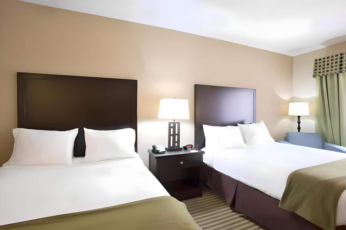 A hotel room with two beds, a nightstand with a lamp, and a window with curtains.