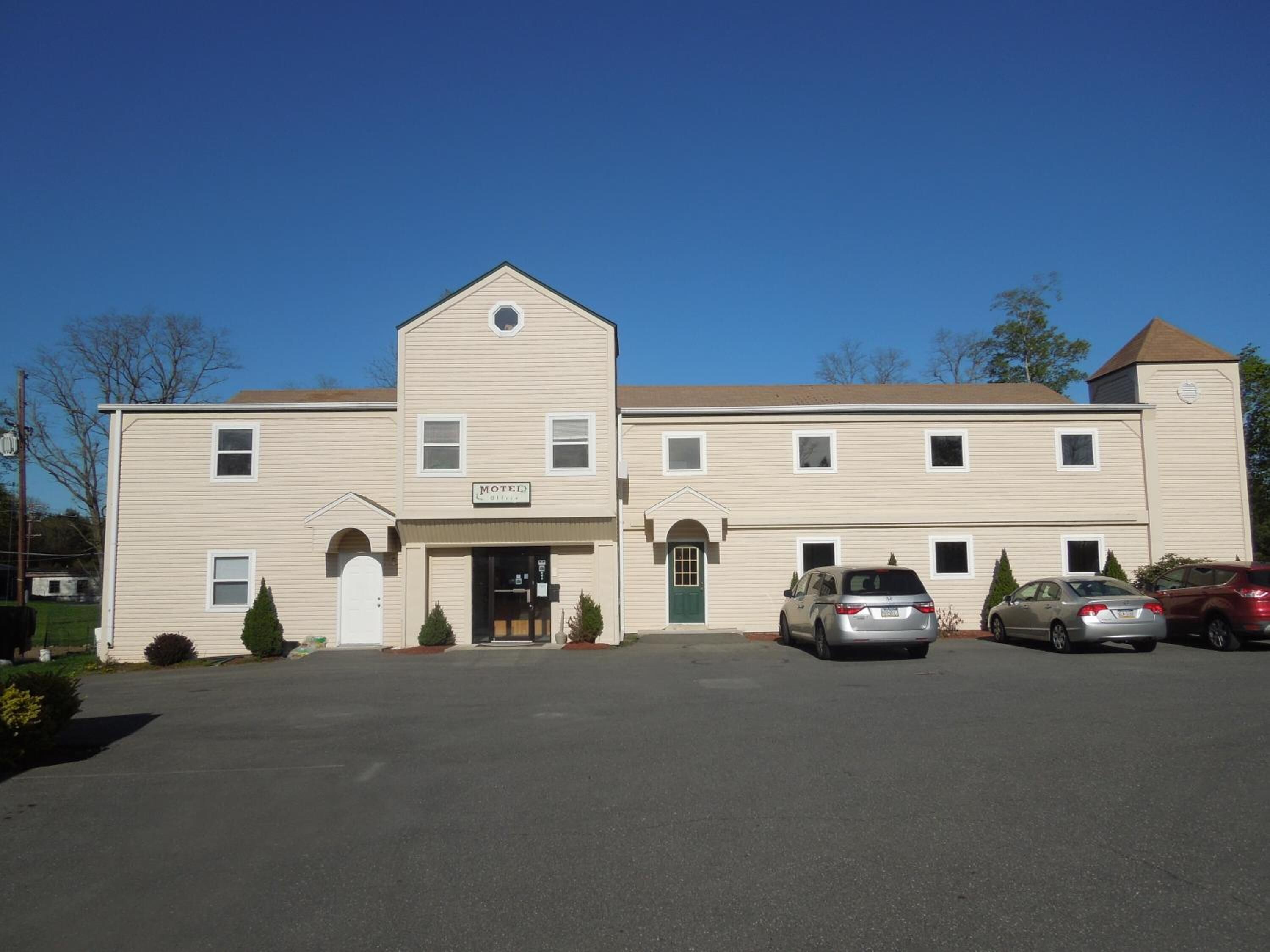 A two-story motel with a central entrance, a small porch, and a parking lot with several cars.