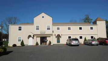 A two-story motel with a central entrance, a small porch, and a parking lot with several cars.