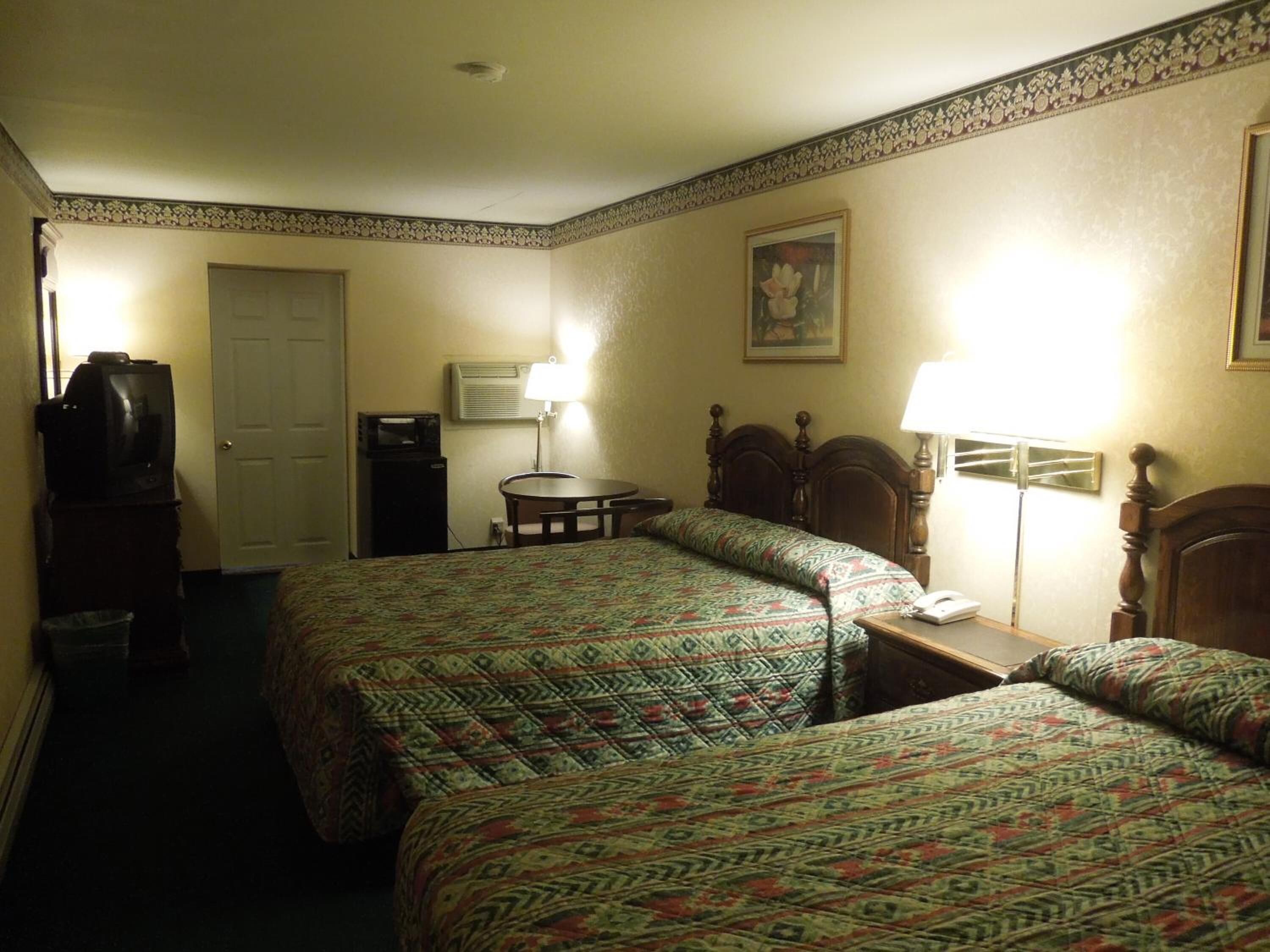Ein Hotelzimmer mit zwei Betten, einem Schreibtisch, einem Stuhl, einem Fernseher, einer Klimaanlage und einem Bild an der Wand.