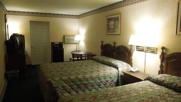 A hotel room with two beds, a desk, a chair, a television, an air conditioning unit, and a painting on the wall.