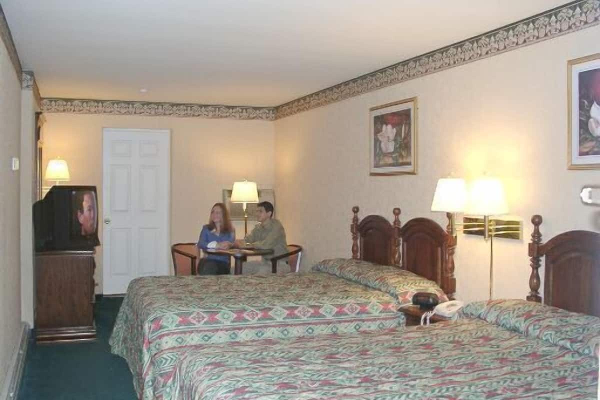 A hotel room with two beds, a desk, and a television.