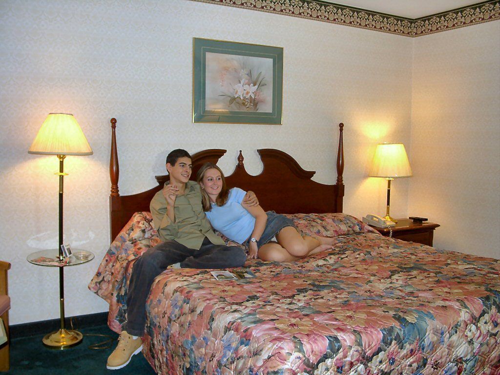 Ein Schlafzimmer mit einem hölzernen Bett, zwei Nachttischlampen, einer blumigen Tagesdecke und einem gerahmten Bild an der Wand.