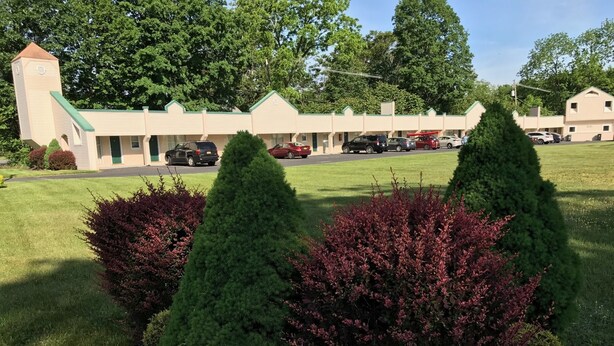 A motel with a row of rooms, a parking lot, and a lawn with shrubs. - Value Inn (East Stroudsburg)