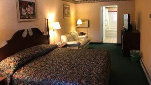 A hotel room with a large bed, a sofa, a TV, and a bathroom visible through an open door. - Value Inn (East Stroudsburg)
