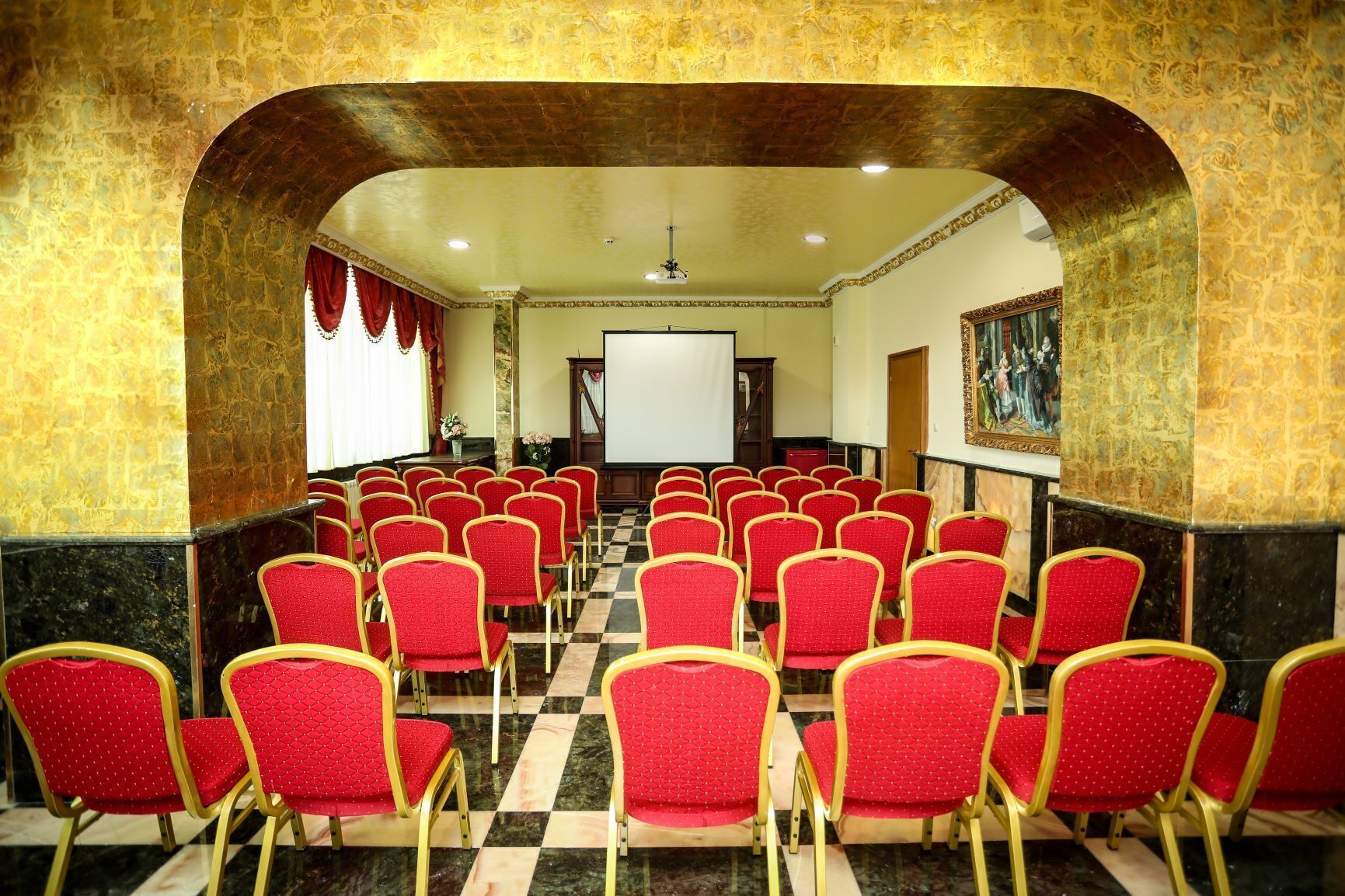 A conference room with rows of red chairs and a projector screen at the front.