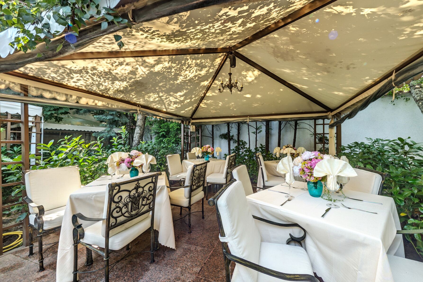 Un patio al aire libre con mesas dispuestas para comer, rodeado de vegetación y cubierto por una gran marquesina.