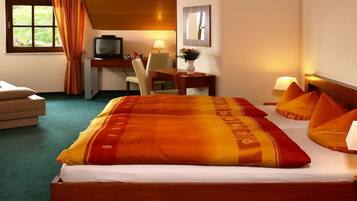 A hotel room with a bed, a desk with a television, a chair, and a window with curtains.