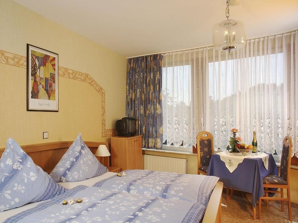 A hotel room with a bed, a television, a dining table with a chair, and a window with curtains.
