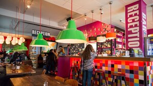 Una zona de bar con mostrador de recepción, paredes de azulejos coloridos y lámparas colgantes verdes.