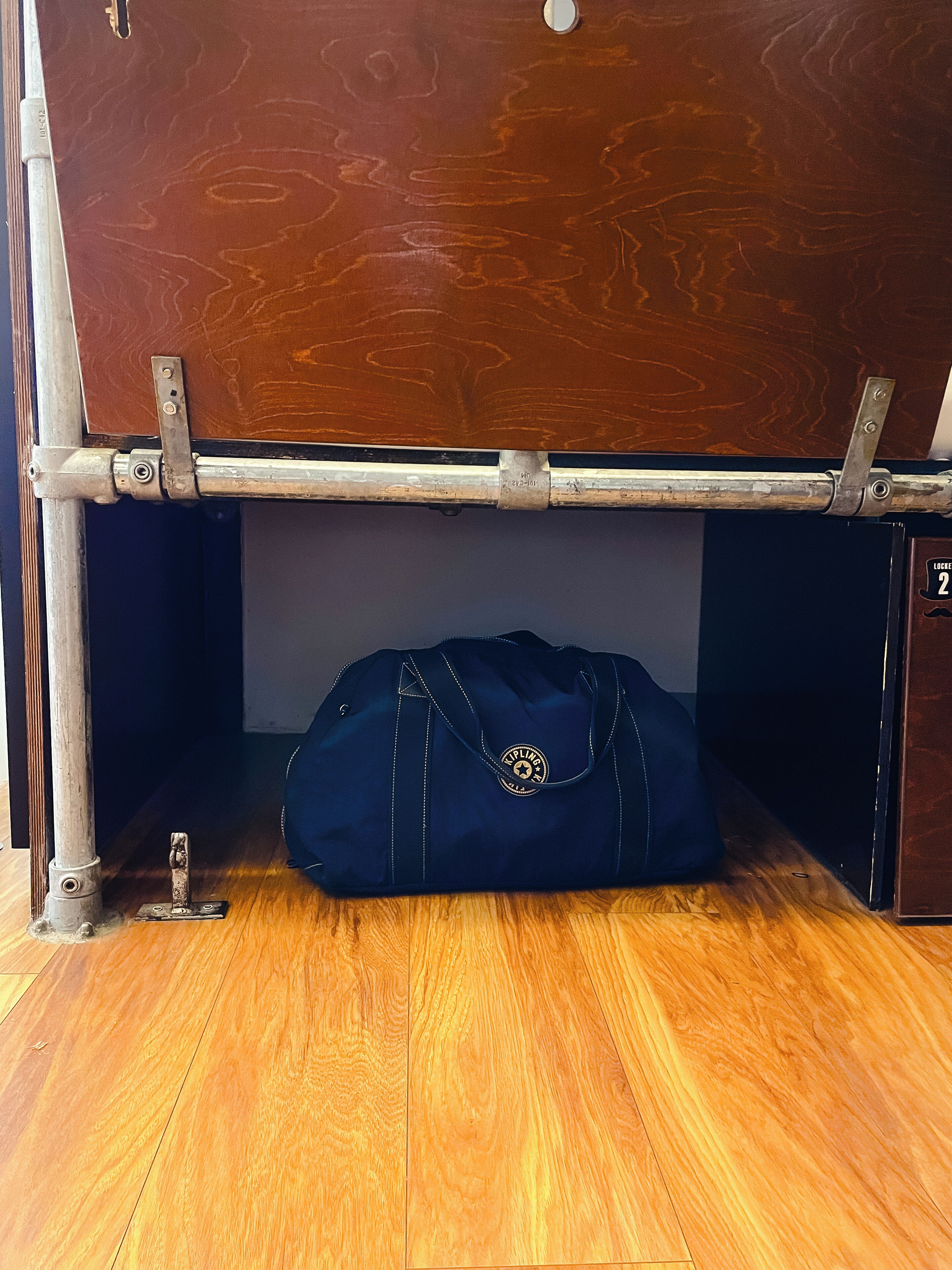 Un plancher en bois, un banc en métal et un sac bleu placé en dessous.