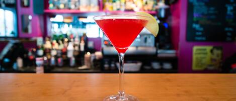 Un verre à martini contenant une boisson rouge et décoré d’une tranche de citron vert, posé sur le comptoir en bois d’un bar.