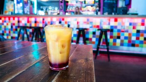 Un bar con una pared de azulejos coloridos y una mesa de madera con un vaso de bebida helada.