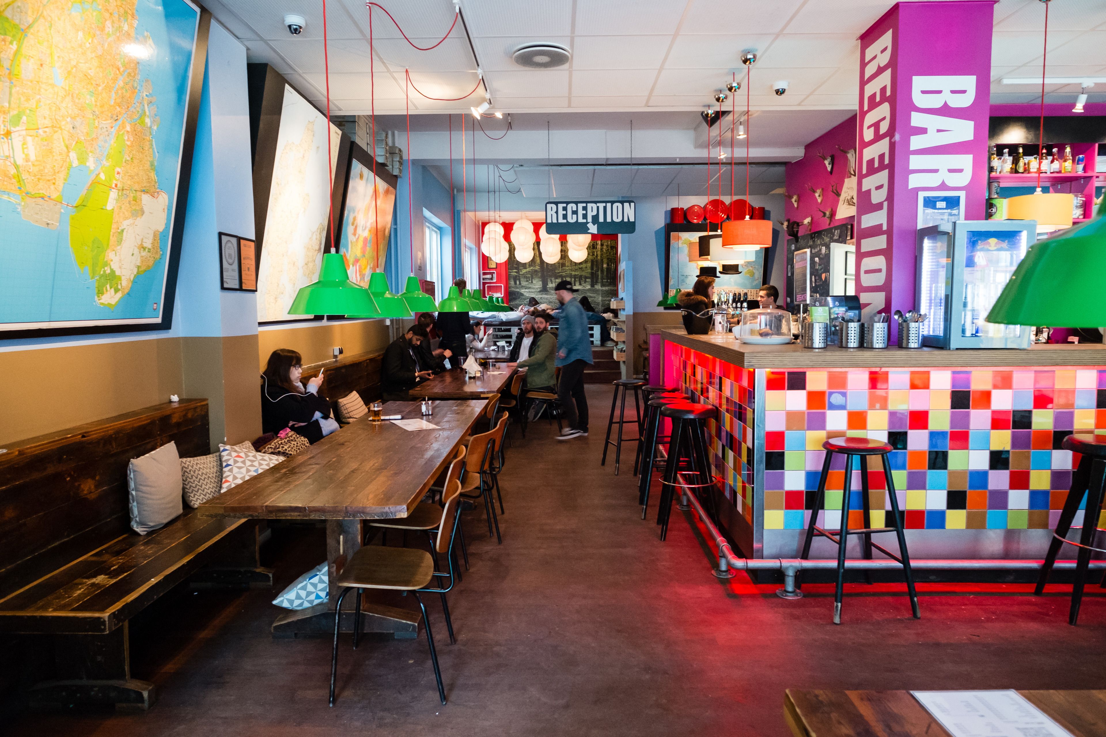 Un interior de restaurante con una zona de recepción, mesas de madera y decoración colorida.