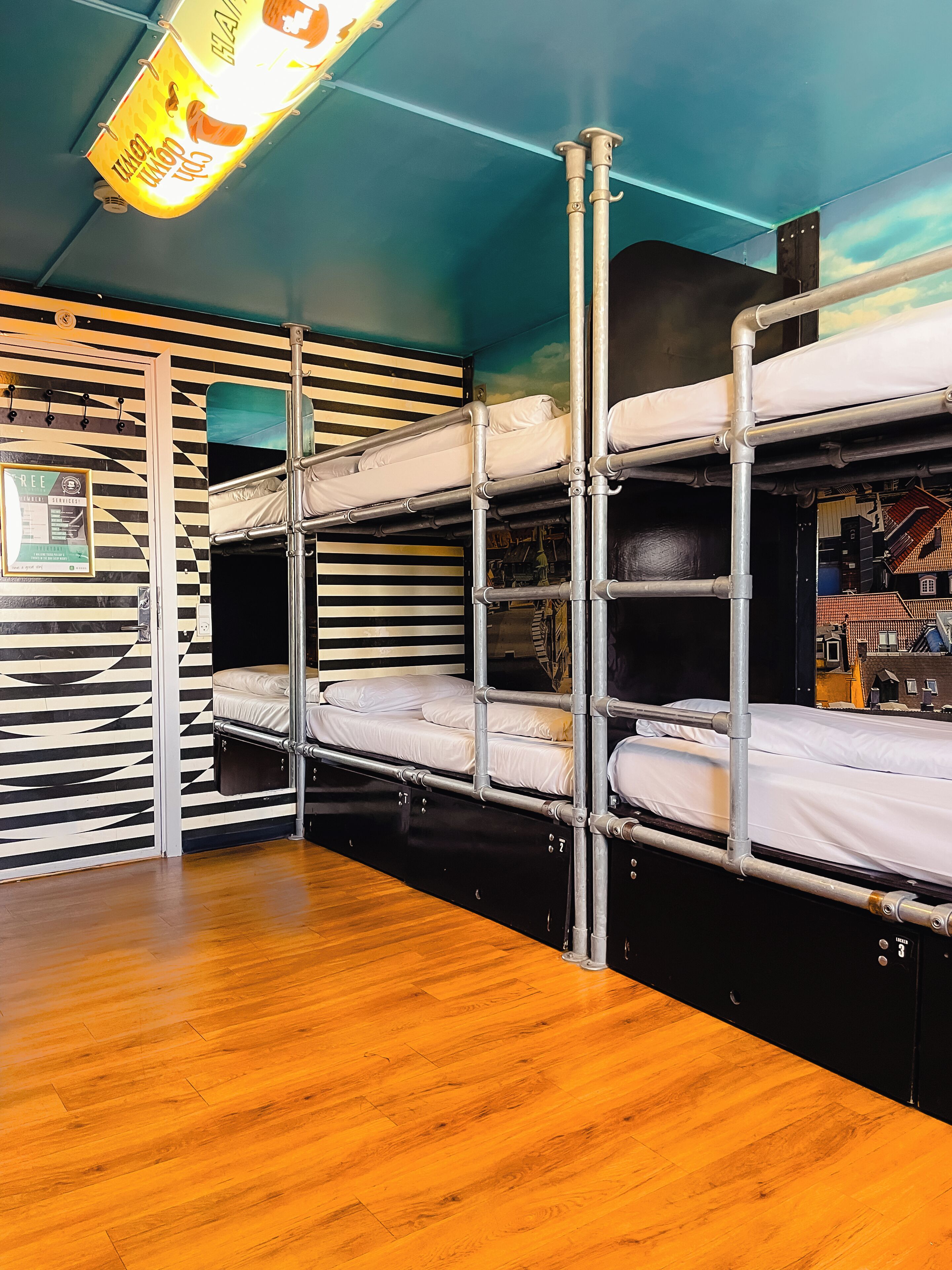 A bunk bed room with a striped wall, a wooden floor, and a ceiling light fixture.